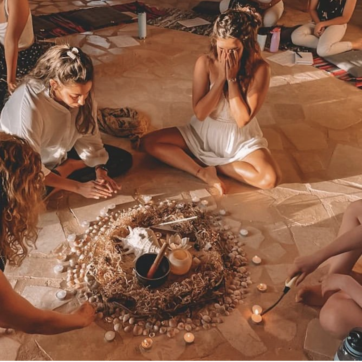 Women sitting together around a candlelit altar of shells, stones and dried flowers during a circle