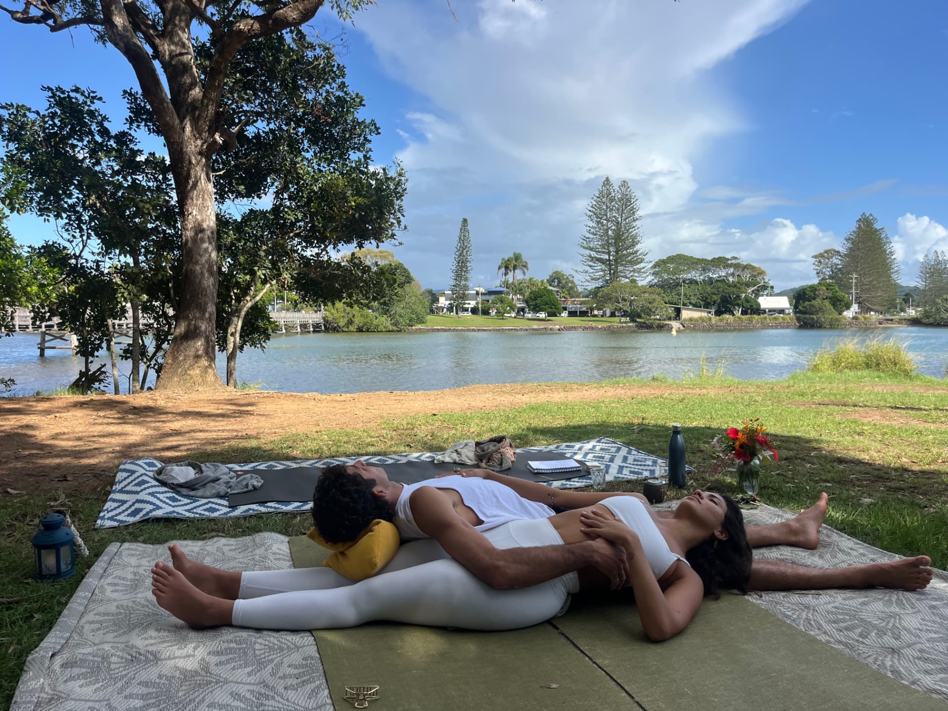 Two people resting together in a peaceful outdoor yoga session by the water